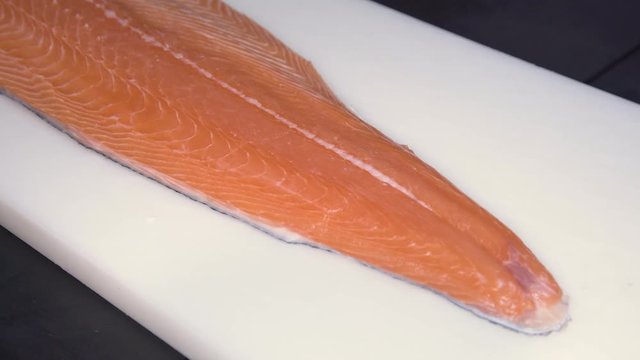 Closeup of a Salmon Fillet on a white cutting board on a black table 
