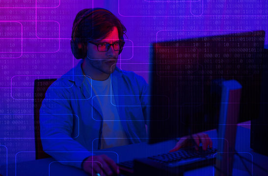Programer in headphones at the computer. Dual screen with binary code