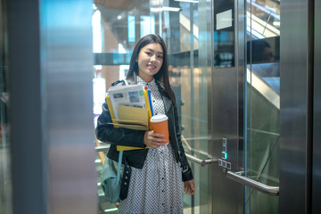 Young dark-haired girl in a black jacket entering elevator and smiling