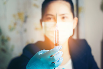Cute female doctor in a medical protective mask holds a syringe with a vaccine in her hands. Against the background is a man in a protective surgical suit and protective medical mask. Coronavirus
