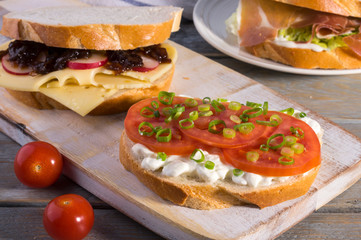Varieties of meat and vegetarian sandwiches on a rustic cutting board.