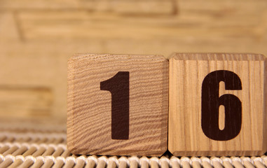 The number sixteen on a wooden cube on a beige background. Cube on a bamboo Mat.