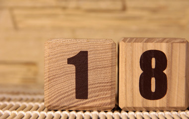 The number eighteen on a wooden cube on a beige background. Cube on a bamboo Mat.