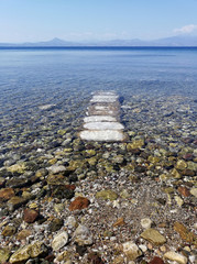 The Ionian sea with clear blue water and mountains on the horizon, stones go into the water like a road