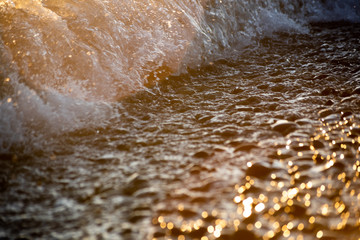 Blurred background with waves in sunlight on pebbles
