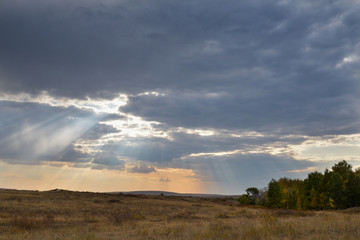 The rays of the sun break through the clouds over field in fall.