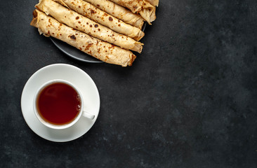 
Homemade breakfast of tea and thin pancakes on a stone background with copy space for your text