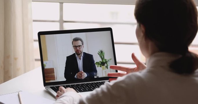 Male executive manager wearing suit consulting female distance client by webcam conference chat. Remote job interview, online business training, professional video call concept. Over shoulder view