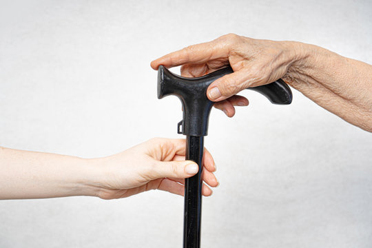 A young hand holds out a walking stick in an old hand.