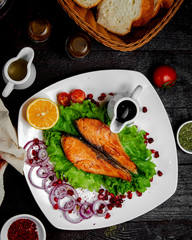 top view of fried salmon fillet served with lettuce red onion rings lemon and pomegranate sauce