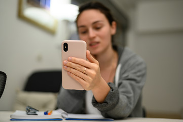 Mobile phone in the foreground. A cute girl in a home environment holds online conferences on her mobile phone. Near a notebook with notes, glasses. Work, study, friendship, friends,sports,online life