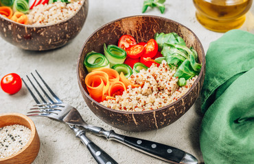 Vegan Buddha bowl. Healthy meal quinoa, tomato, cucumber, carrot, radish, corn salad in coconut bowls on concrete background. Selective focus