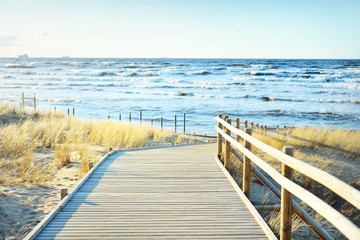 A wooden pathway to the Baltic sea at sunset. Sand dunes and plants in the background. Clear blue...