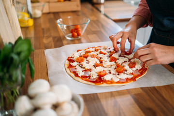 Woman's hands adding cherry tomatoes to a traditional margarita pizza. Preparation of a Original Italian pizza