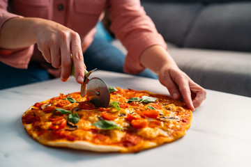 Woman cutting a traditional italian margarita pizza in her living room. Stay at home