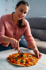Woman cutting a traditional italian margarita pizza in her living room. Stay at home