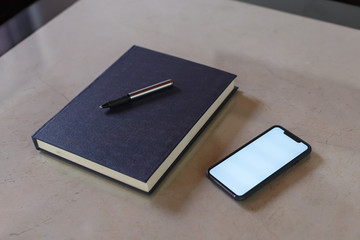 Notebook with pen next to a cell phone over a glass table for home office