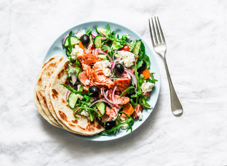 Roasted salmon, tomato, cucumber, rocket, feta cheese greek salad on a light background, top view. Healthy mediterranean diet food concept