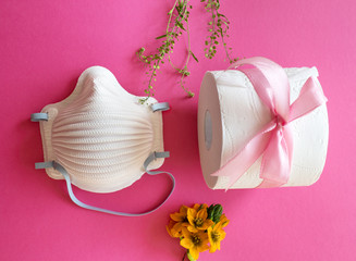 Toilet paper roll and a medical face mask isolated on pink coloured background