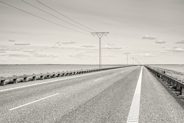 Asphalt highway crossing the sea. Monochrome, black and white landscape photography.
