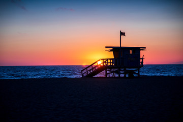 A lifeguard stands sits in silhouette as the skies explode in color during sunset in Hermosa Beach, California.