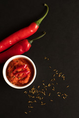 Harissa sauce in a gravy boat. Ingredients for cooking - chili peppers and spices. Black background top view
