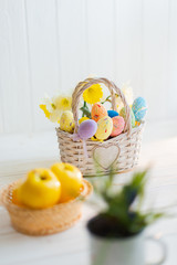 Multi-colored Easter eggs in a basket on a white wooden background