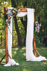 arch for the wedding ceremony, decorated with cloth flowers and greenery, is in park