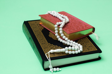 Two Quranes of blue and pink color with muslim rosary on a green background