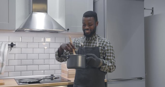 Man stirring cooked soup in pan wearing apron at kitchen preparing dinner