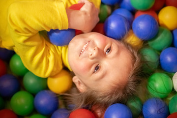 Fototapeta na wymiar Little girl in a ball pit smiling at the camera, having fun at the children play center