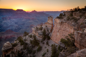 Sun sets over the Grand Canyon as silhouettes of people overlook from afar