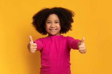 Cute little black girl showing thumbs up and smiling at camera