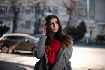 Girl in a red blouse and a gray cardigan on a blurry city background in early spring