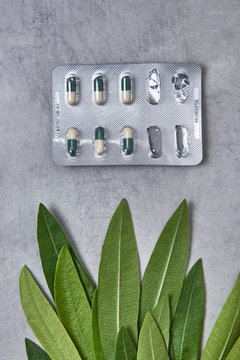 Blister de pastillas sobre fondo gris de marmol o cemento y hojas verdes