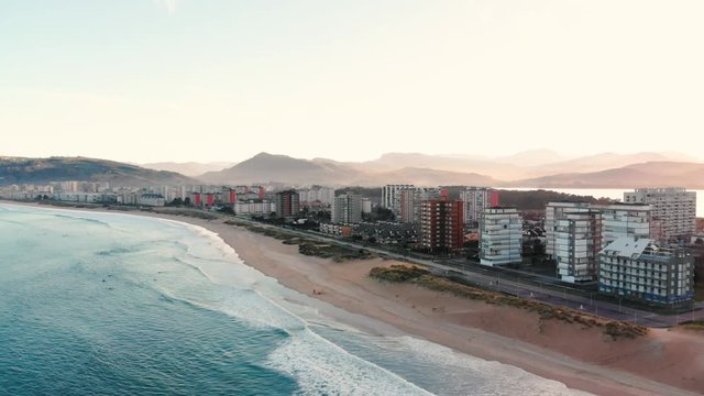 Circular aerial drone view of a coast skyline village next to the sea. Beach bay sunset with dunes in Laredo. Ideal for surfing.