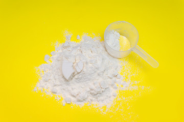 Heap of protein powder with plastic spoon on yellow background