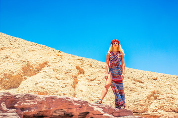 sexy adorable girl portrait in fashion drees looking from below domination sight in desert bright vivid colorful nature warming environment blue sky background