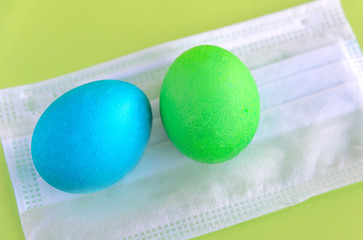 Easter eggs lie on a medical mask, on a green background. The concept of the Easter holiday during the epidemic of the coronavirus COVID-19
