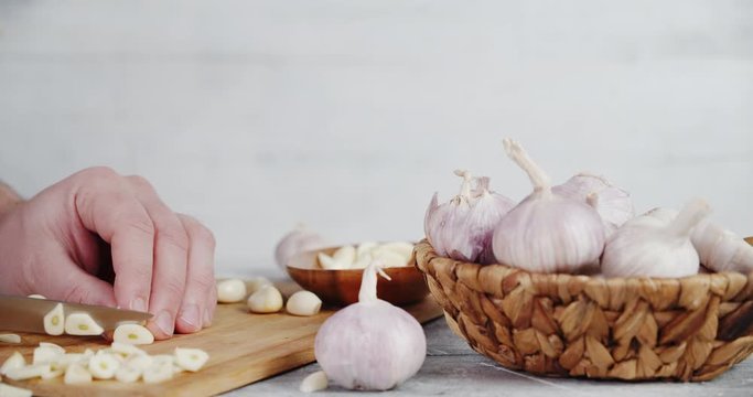 Men hands cut with a knife the garlic into small pieces on a cutting Board.