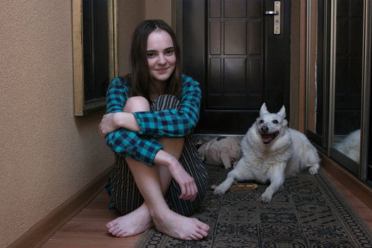 beautiful long-haired teenager girl sitting on the floor in the hallway with a white West Siberian Laika husky. The dog cannot or is about to go for a walk outside. Self-isolation in the apartment wit