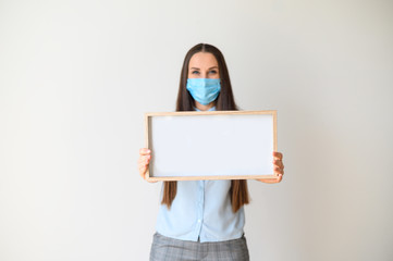 Fototapeta premium Woman in a medical mask stands with a blank board