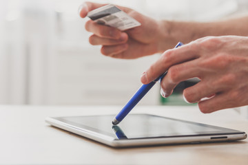 Man using pc tablet with stylus and credit card at the table, shopping online
