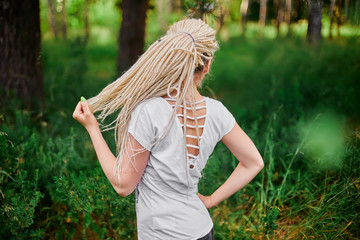 blonde girl with dreadlocks doing yoga in the park on the rug