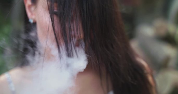 girl with blowing hair smoking e-cigarette and exhales into camera
