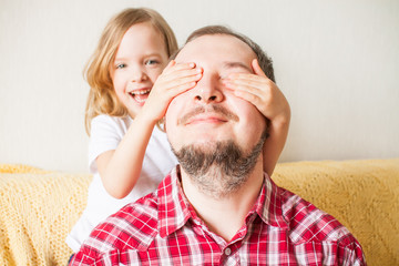 Little girl wishes dad happy father's day. Daughter hugs dad, closes his eyes with his hands