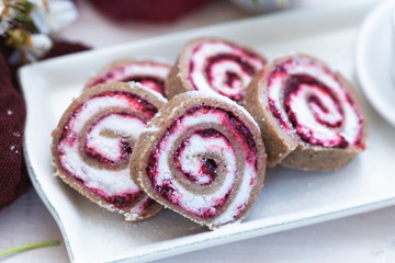 Vegan raw raspberry rolls with coconut flour on a white table with spring flowers and red silk. Vegan cookies with birch sugar on a white plate.