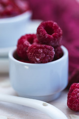 Fresh raspberries in a white cup on a white wooden table top. Raw vegan food. Red colored fruit. 