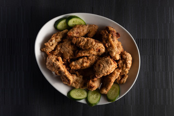Fried Chicken with Cucumbers on a white plate on a dark background