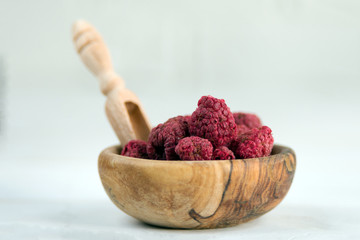 Dried raspberries in a wooden bowl on a white background. Dried berries are a useful product for...